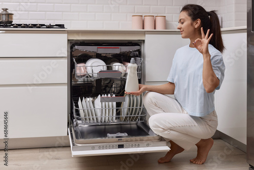 Quadro em tela woman pours rinse aid into the dishwasher compartment in modern white kitchen