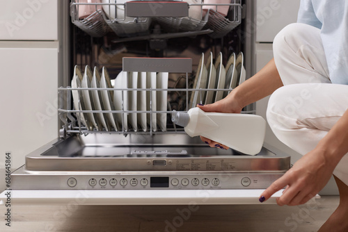 Canvas Print female hand pours rinse aid into the dishwasher compartment in modern white kitc