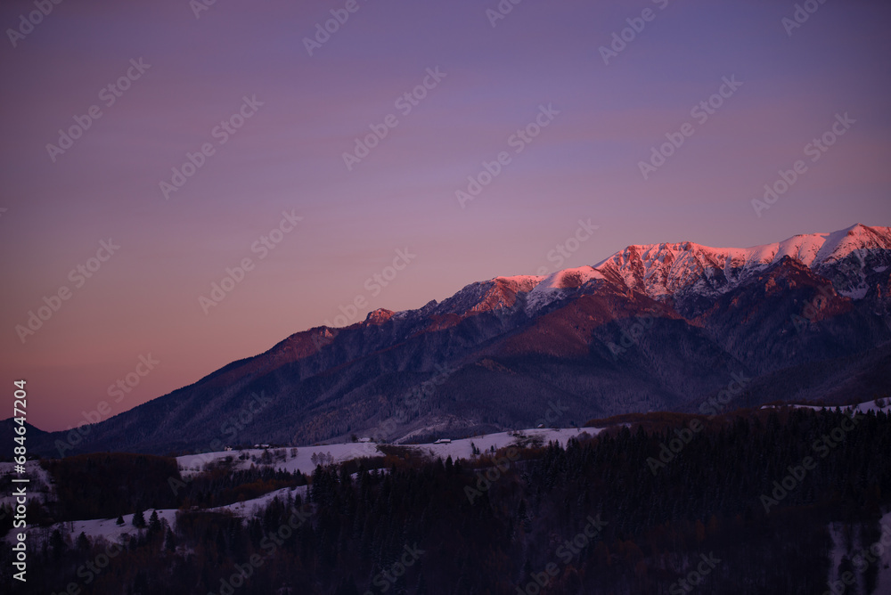Winter landscape with high and snowy rocky mountains. Amazing sunset in shades of purple in the evening sky Winter landscape with high and snowy rocky mountains. Amazing sunset in shades of purple in the evening sky