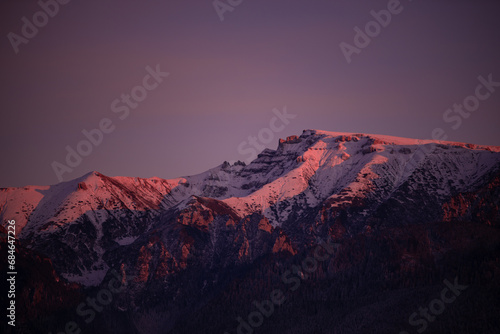 Winter landscape with high and snowy rocky mountains. Amazing sunset in shades of purple in the evening sky © badescu