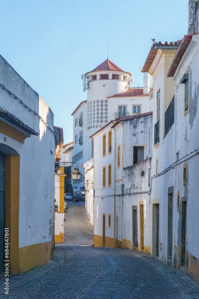 The view of narrow paved street of Evora with the cozy white and yellow houses, Evora, Alentejo, Portugal