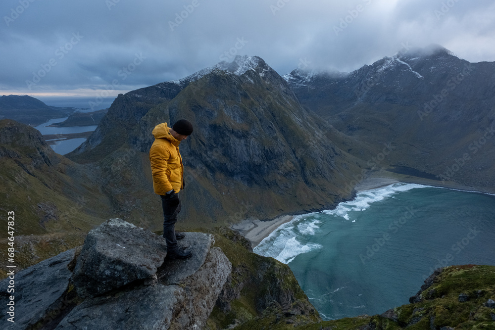 Man in yellow jacket at Kvalvika Beach at sunset in Lofoten, Norway in the Arctic Circle.  One of Norway's most beautiful beaches. with tower cliffs and large waves.