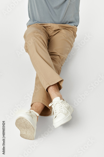 guy with crossed leg wearing white sneakers and beige pants sitting on floor