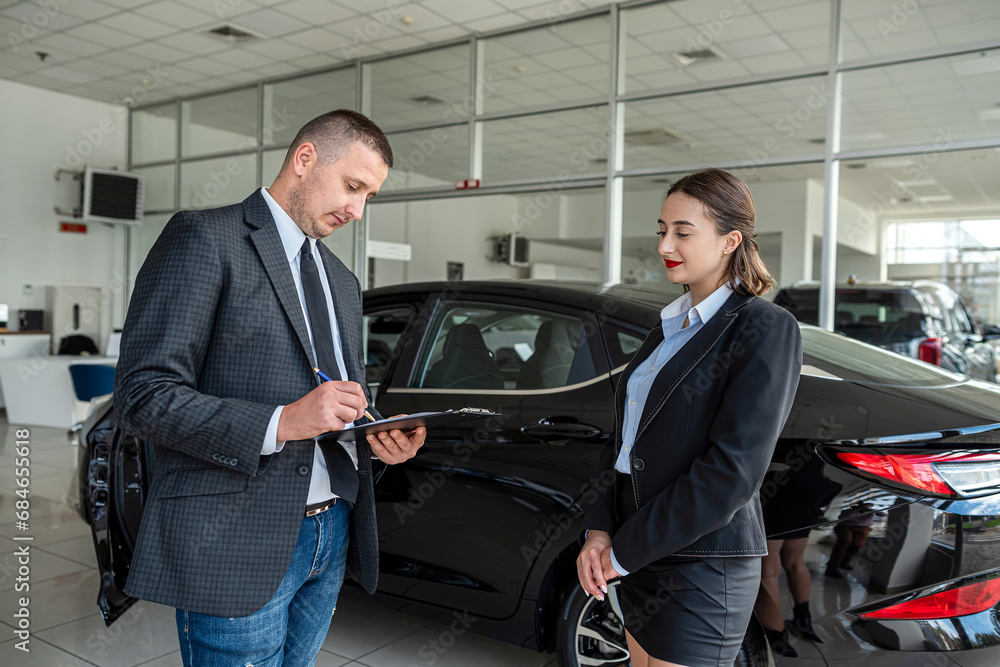 young manager in suit holding clipboard with female client talking to sales modern car young manager in suit holding clipboard with female client talking to sales modern car