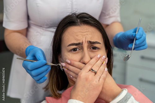 Scared young woman closes her mouth with her hands at the dentist s appointment