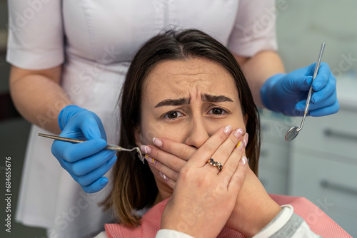 фотографія Scared young woman closes her mouth with her hands at the dentist's appointment
