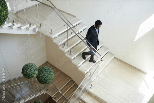 High angle view at Black man in business suit going downstairs holding on handrail in modern office building, copy space photo