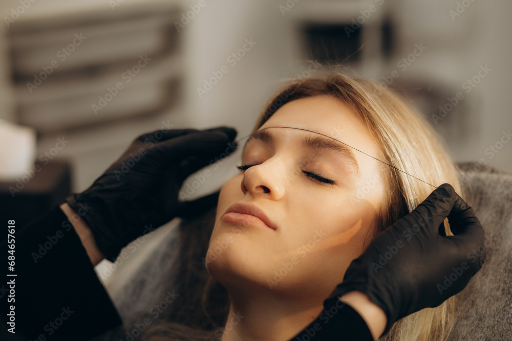 Fototapeta premium Marking of eyebrows. Permanent brow makeup. Markings with white paste and measuring ruler. Permanent make up artist in black gloves