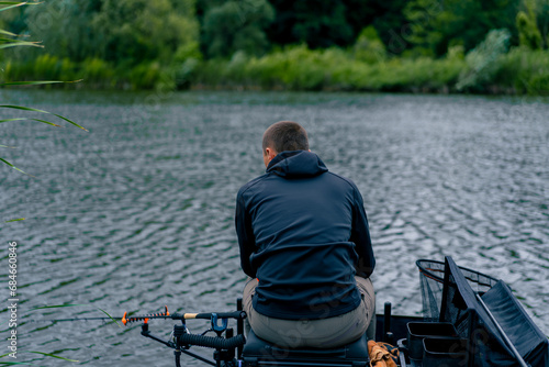 Fisherman with fishing rod or spinning and professional tools sitting on the river bank rear view Pull fish out of the lake sports fishing photo