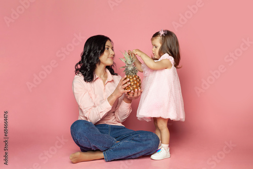 Young brunette woman and baby girl holding fruit on pink background photo