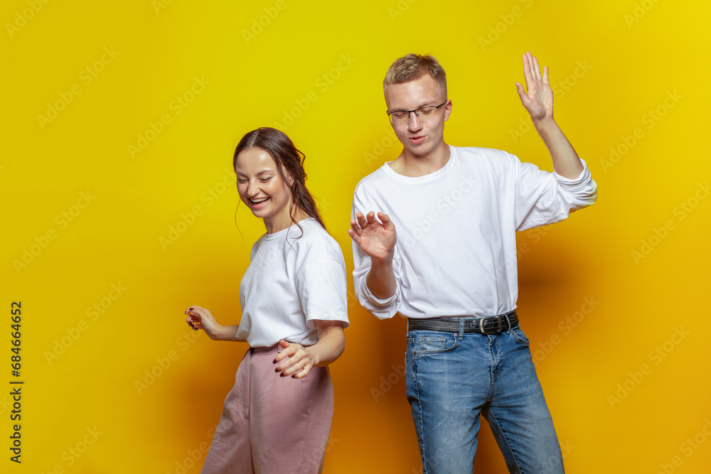 Happy laughing couple in casual wear dancing against yellow studio wall background Happy laughing couple in casual wear dancing against yellow studio wall background