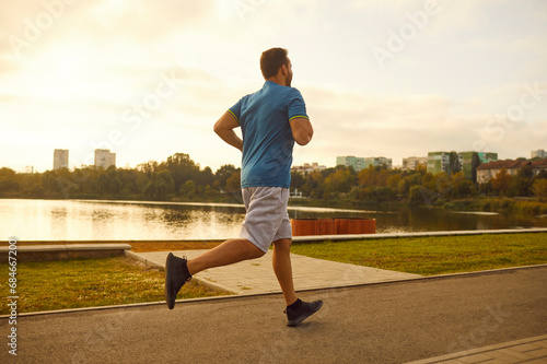 Fototapeta Naklejka Na Ścianę i Meble -  Young sporty male runner jogging in city park along river. Healthy sporty fitness man running outdoors training for wellness, health and cardio. Workout in nature and healthy lifestyle concept.