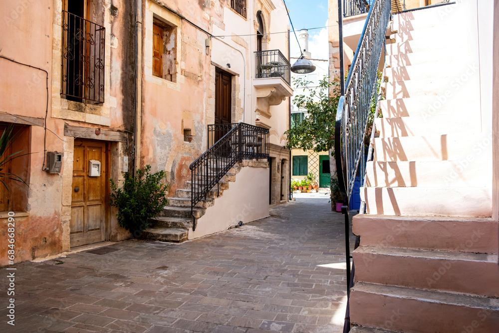 Chania Old Town, Crete island Greece. Traditional weathered building with stair, plant, paved alley.