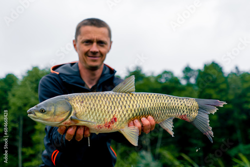 portrait of a satisfied professional fisherman holding a carp on the bank of a river fishing in a pond with a good catch