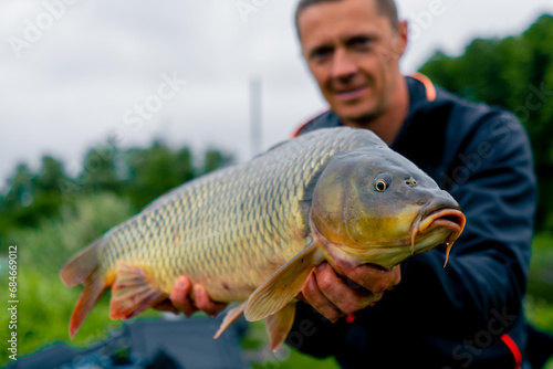 portrait of a satisfied professional fisherman holding a carp on the bank of a river fishing in a pond with a good catch