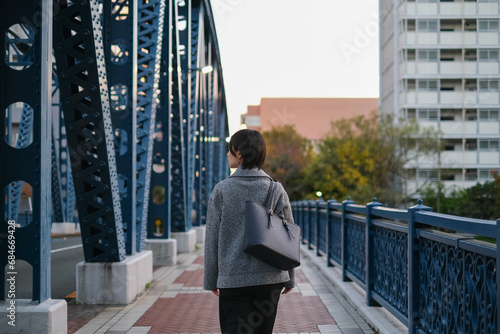 青い橋の上を歩く女性の後ろ姿