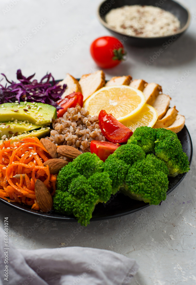 The concept of proper, nutritious nutrition, a bowl with chicken breast, buckwheat, vegetables, cabbage, broccoli, carrots, nuts, avacado and cherry tomatoes, On a light background, close up. The concept of proper, nutritious nutrition, a bowl with chicken breast, buckwheat, vegetables, cabbage, broccoli, carrots, nuts, avacado and cherry tomatoes, On a light background, close up.