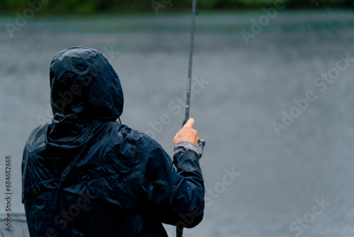 Obraz na plátne Fisherman in raincoat with fishing rod or spinning and professional tools sittin