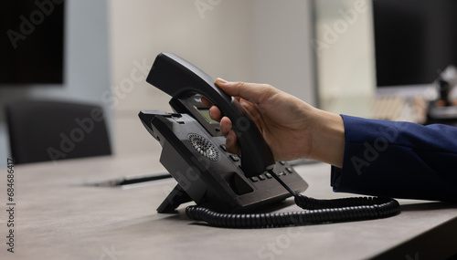 close up man hand touching telephone for call  or connecting with partner,vendor or customer at computer desktop operation room, hotline and helpline concept. photo