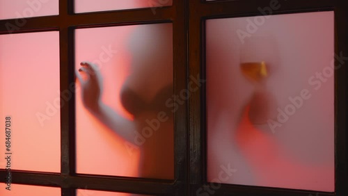 Unrecognized nude model shows glass of wine behind matt glass at sunset, slow mo. Seductive girl, young flexible lady with perfect body, moving shadow, silhouette. Slow motion high quality 4k footage