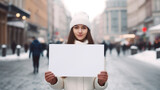 Młoda dziewczyna trzyma kartkę papieru, biały plakat z miejscem na treść w centrum miasta na ruchliwej ulicy.