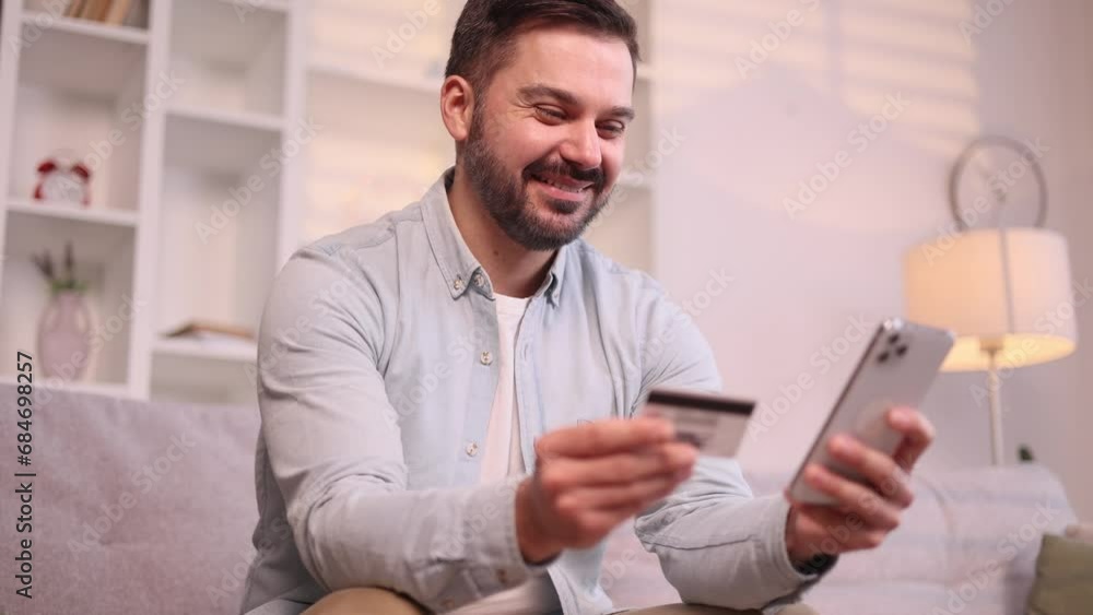 Portrait of bearded handsome man paying with credit card on smartphone cellphone at home Happy customer doing payments online shopping in internet store and receiving cashback Easy pay concept Portrait of bearded handsome man paying with credit card on smartphone cellphone at home Happy customer doing payments online shopping in internet store and receiving cashback Easy pay concept