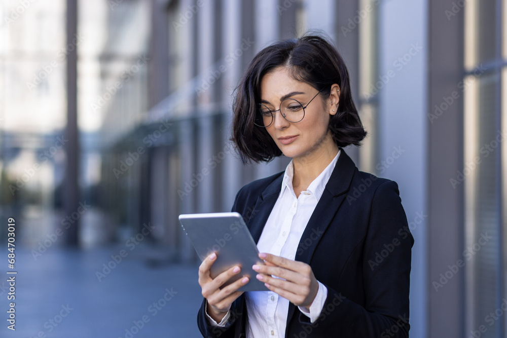 Close-up photo of serious young businesswoman talking on the street near work office on video call on tablet, watching and developing project, startup, waiting for meeting