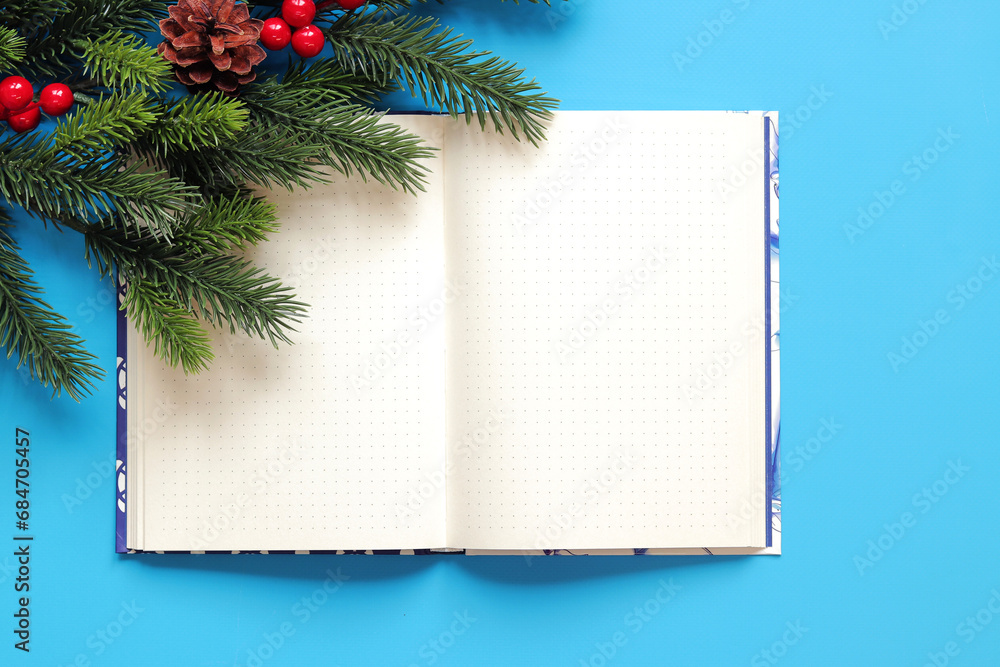 Open notebook on a blue background, spruce branch, top view, empty space. Copy space. Christmas branch and diary for notes Open notebook on a blue background, spruce branch, top view, empty space. Copy space. Christmas branch and diary for notes
