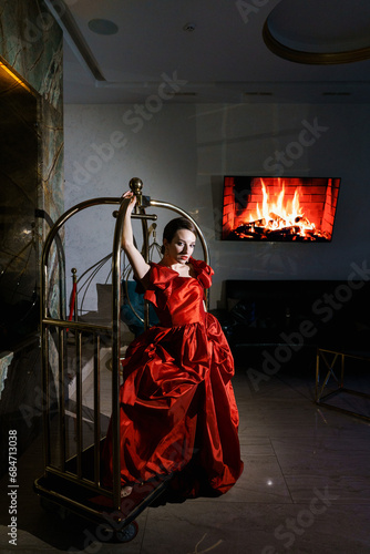 Pretty woman in a luxurious red dress posing in a luggage trolley.Fashion shooting concept