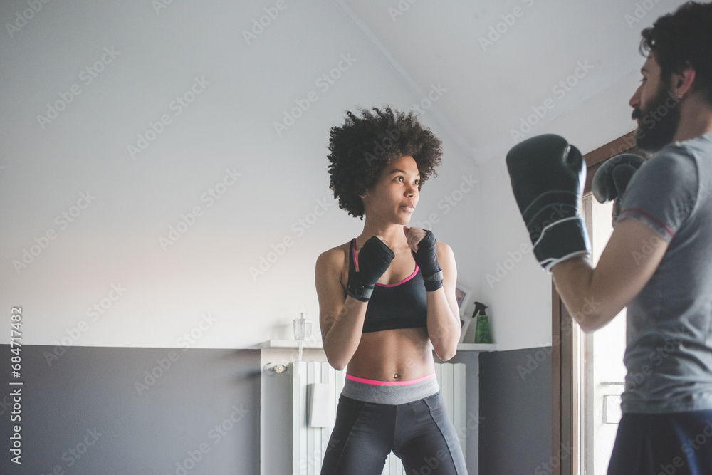 Young multiethnic woman at home training with coach doing boxe exercise - obrazy, fototapety, plakaty 