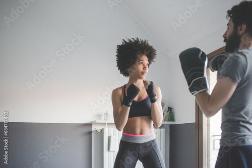 Young multiethnic woman at home training with coach doing boxe exercise photo