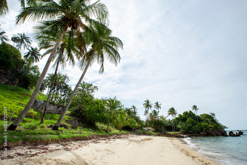 Praia deserta em ilha com coqueiros e casa abandonada