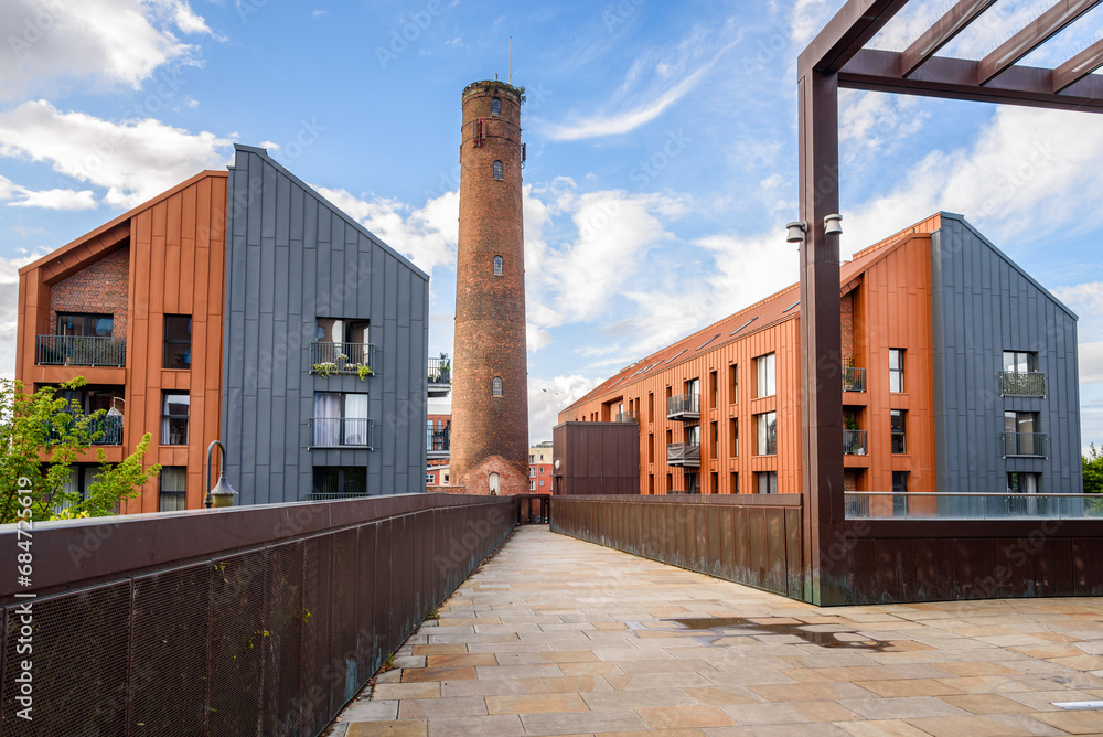 Deserted footbridge leading to two modern apartment buildings overlooked by a old brick tower on a sunny summer day Deserted footbridge leading to two modern apartment buildings overlooked by a old brick tower on a sunny summer day