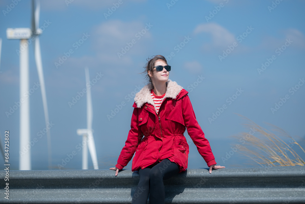 Obraz premium On the background of windmills, A young woman in a red jacket is enjoying her winter vacation.