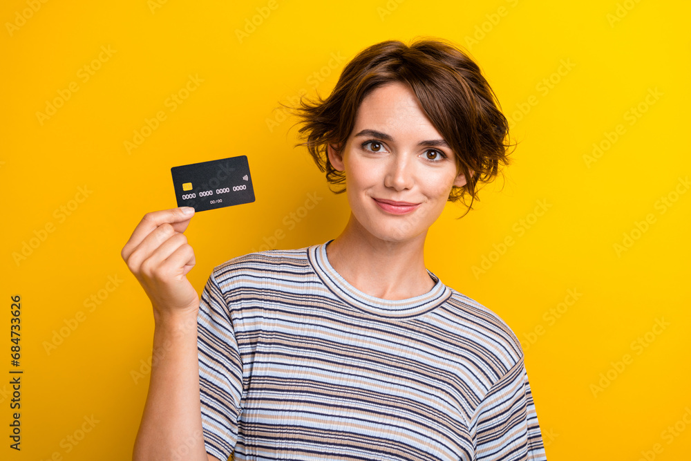 Portrait of satisfied intelligent adorable girl wear grey t-shirt demonstrate plastic card in hand isolated on yellow color background Portrait of satisfied intelligent adorable girl wear grey t-shirt demonstrate plastic card in hand isolated on yellow color background