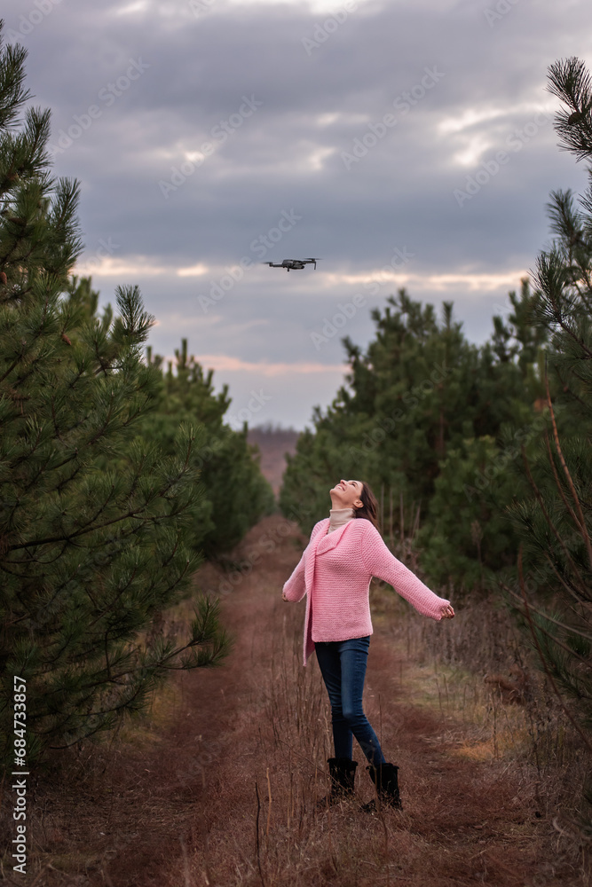 Young woman in knitted pink in countryside among coniferous trees in forest posing for drone camera