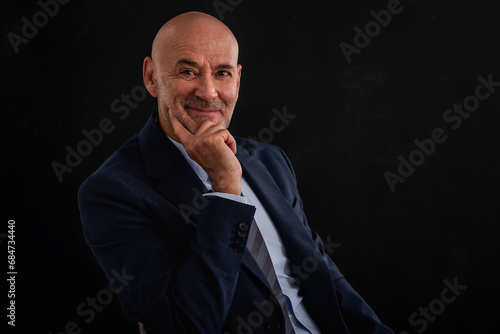 Portrait of mid aged businessman sitting against isolated black background © gzorgz