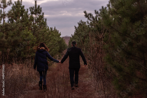 Happy couple running through forest holding hands. Man in coat and a young woman are fooling around © farmuty