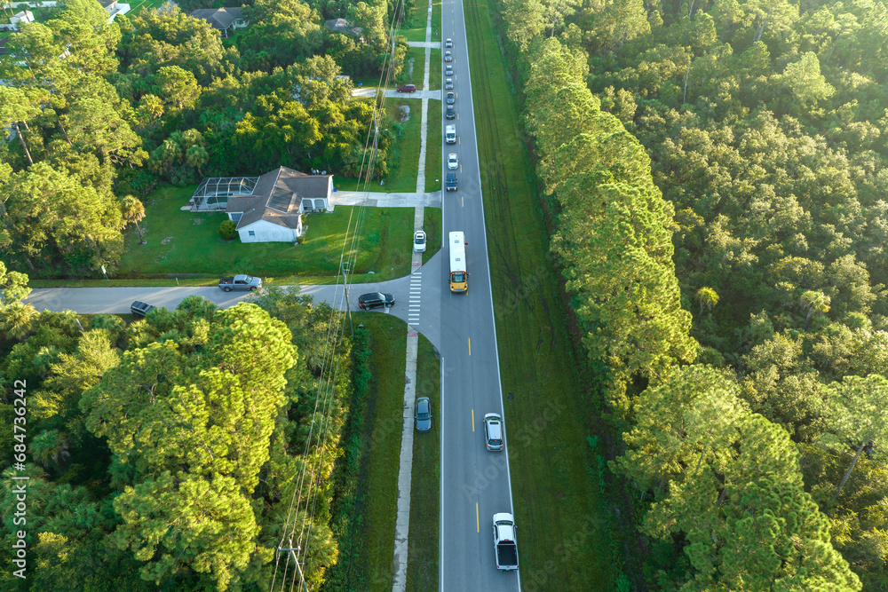 Top view of standard american yellow school bus picking up kids at rural town street stop for their lessongs in early morning. Public transport in the USA