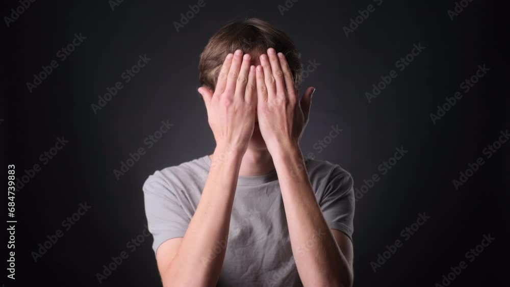 Serious Caucasian Man Covering Face with Hands on black Background Serious Caucasian Man Covering Face with Hands on black Background