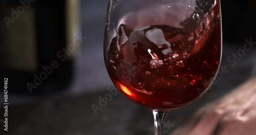 Super slow motion macro of fine quality red wine poured in transparent glass is being checked of quality by male winemaker or sommelier in wine cellar. photo