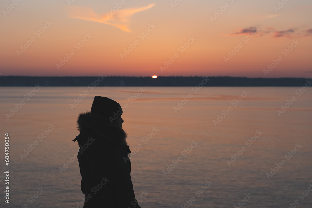Silhouette of a girl in winter at sunset by the sea.