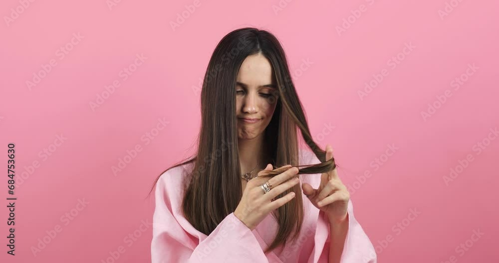 Depressed young woman looking at split brunette hair ends. Worried sad girl feels upset about brittle damaged dry hair loss concept. Female hormone problems concept isolated pink background. Depressed young woman looking at split brunette hair ends. Worried sad girl feels upset about brittle damaged dry hair loss concept. Female hormone problems concept isolated pink background.