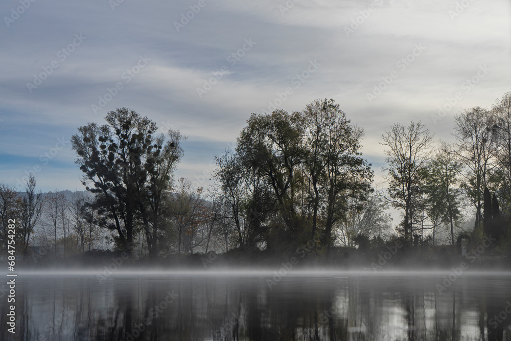 Small lake with fog patches and trees in autumn Small lake with fog patches and trees in autumn