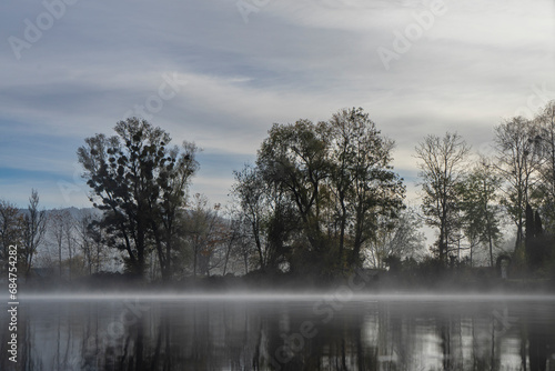 Small lake with fog patches and trees in autumn