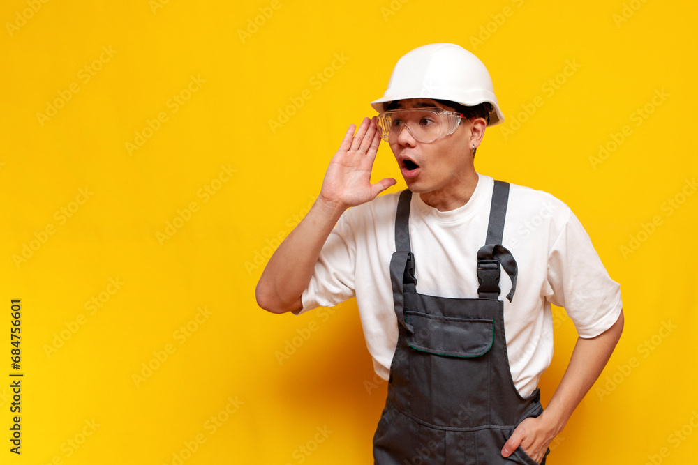 asian male builder in uniform announces information on yellow isolated background