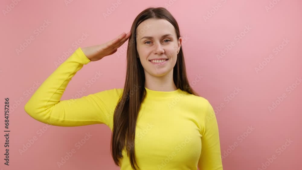 Portrait of serious cute young woman standing saluting with hand near head, looking obedient and attentive at camera, wearing yellow sweater, posing isolated over pink color background wall in studio Portrait of serious cute young woman standing saluting with hand near head, looking obedient and attentive at camera, wearing yellow sweater, posing isolated over pink color background wall in studio