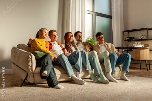 multiracial group of young friends sitting on sofa at home hugging and looking at camera photo