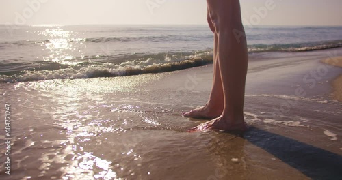 Close-up shot of legs woman stand on sea beach at sunset, low angle shot photo