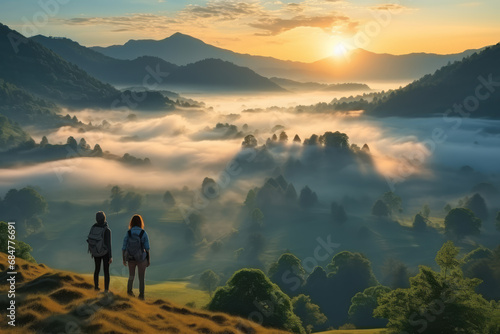 A couple hikers enjoy the dramatic view of the sunrise over a sea of clouds and mountains on a holiday. Concept suitable for mountain climbing, hiking and inspiration. © omune